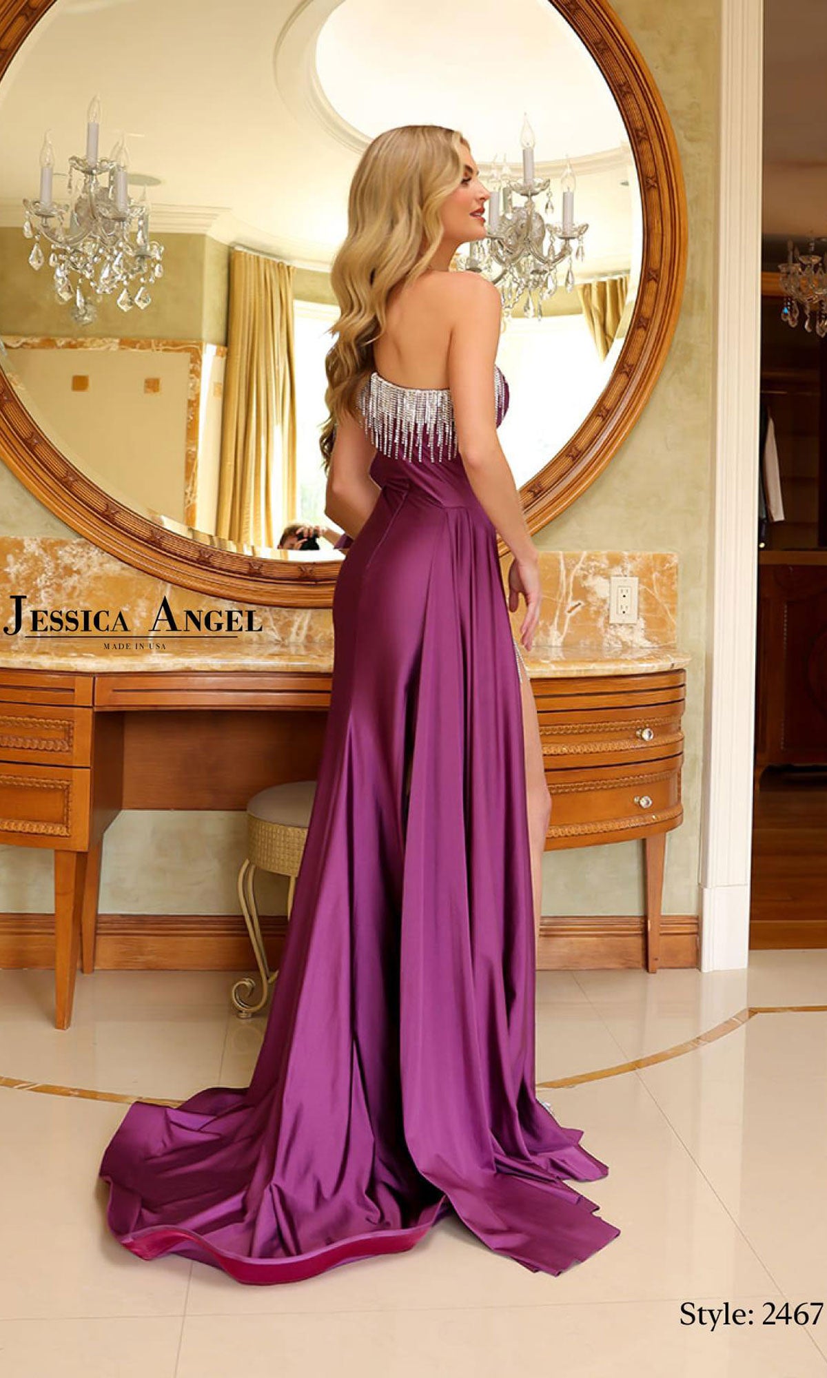 A woman wearing the Jessica Angel 2467 One-Shoulder Long Prom Dress with silver fringe poses in front of a vanity and round mirror in an elegant room.